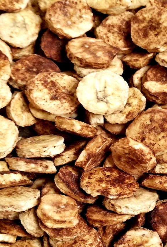 Picture of sliced choco banana chips in a bulk container. Choco Banana Chips are freeze dried banana slices generously sprinkled with a cocoa powder blend.