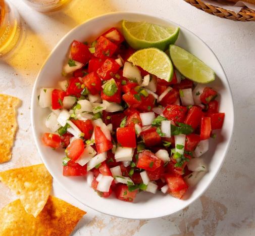 pico de gallo in a white bowl with lime wedge garnish next to chips